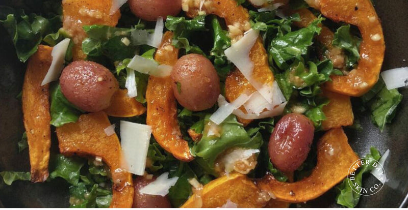 A vibrant warm squash salad featuring roasted butternut squash, kale, seedless red grapes, and shaved Parmesan, beautifully presented in a rustic bowl.