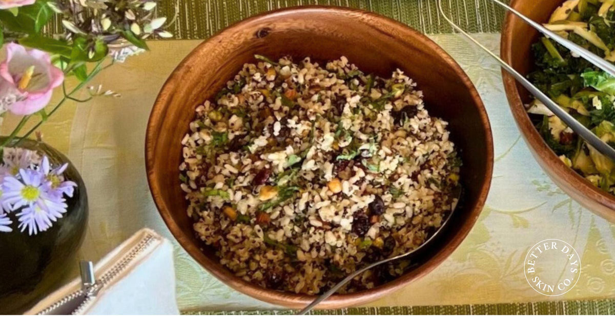 A colorful bowl of warm wild rice salad featuring wild rice, short-grain rice, currants, and a variety of nuts, garnished with fresh herbs and beetroot, all beautifully presented.