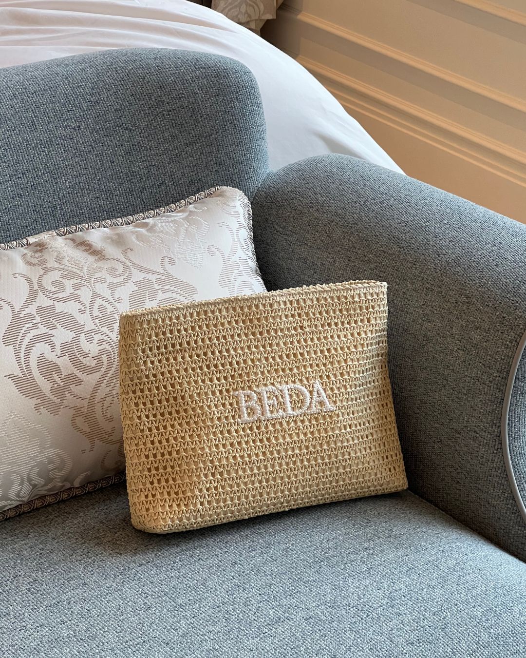Raffia travel pouch with 'BEDA' branding a hotel bedroom suite
